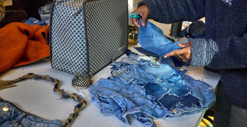 Vrouw is op een tafel bezig met het naaien van spijkerstof