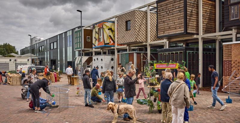 Op de foto De HER met onder andere de tien circulaire boxen. Op de voorgrond diverse mensen die een bezoek brengen aan De HER.