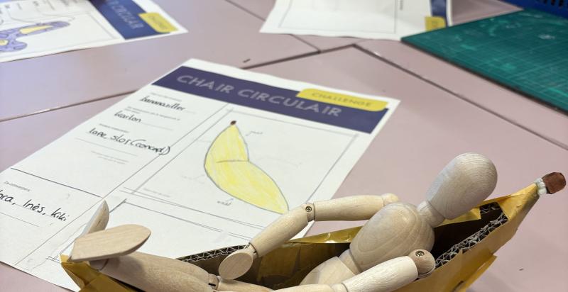 Een houten poppetje ligt in een schaalmodel van een relaxte stoel.