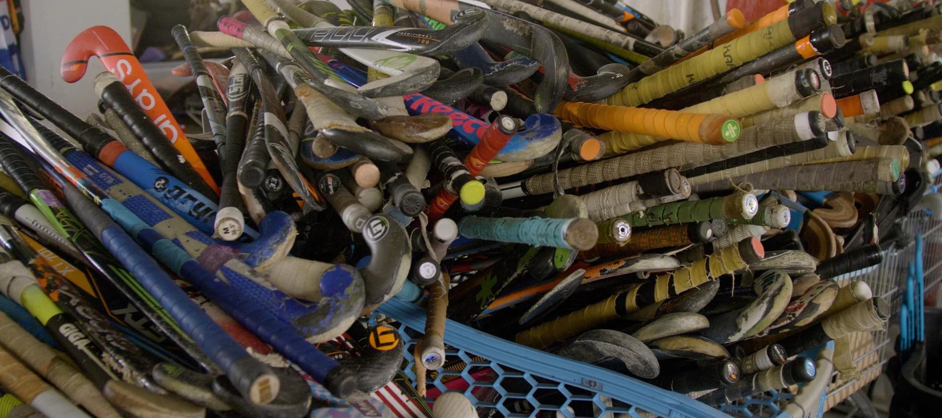 heel veel oude hockeysticks (meer dan 100) op elkaar in een blauw winkelwagentjes