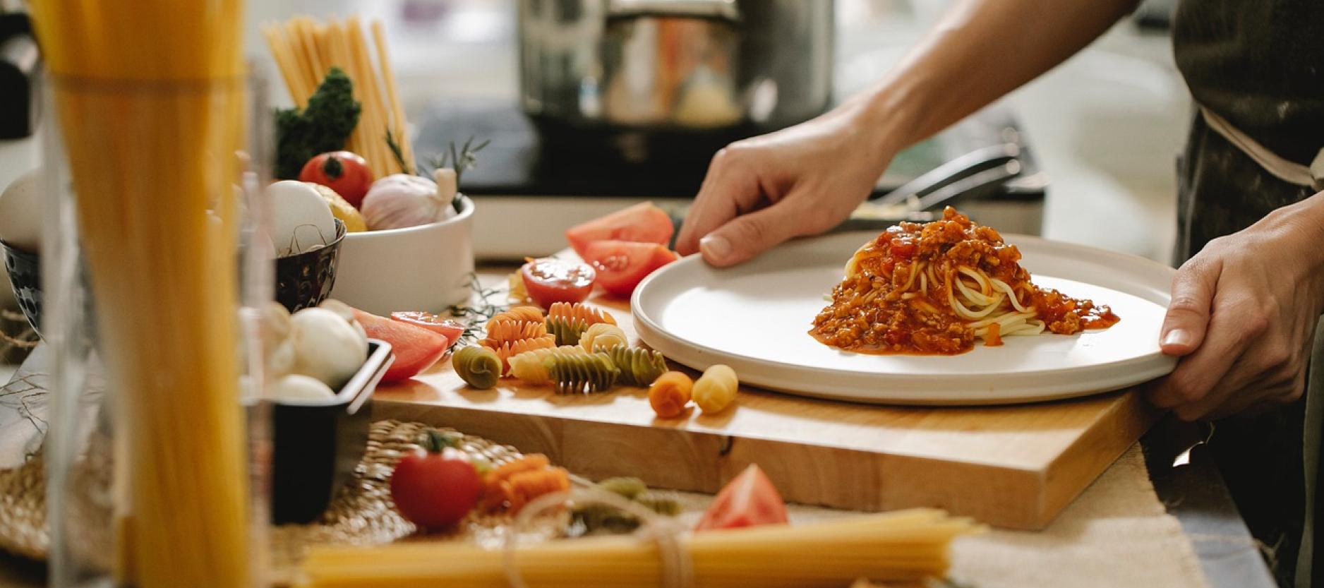 Close up van een wit bord met spaghetti. Eromheen liggen verschillende ingrediënten zie zijn gebruikt.