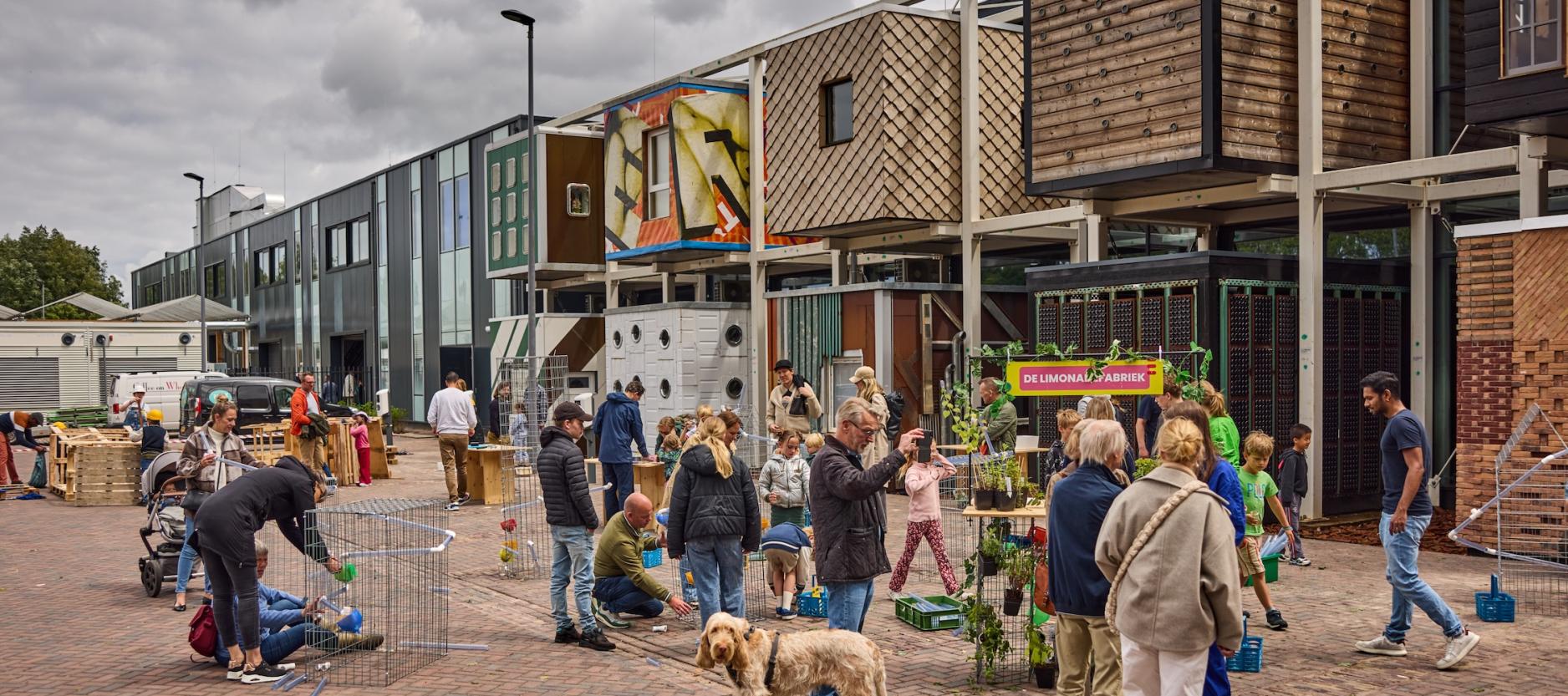 Op de foto De HER met onder andere de tien circulaire boxen. Op de voorgrond diverse mensen die een bezoek brengen aan De HER.