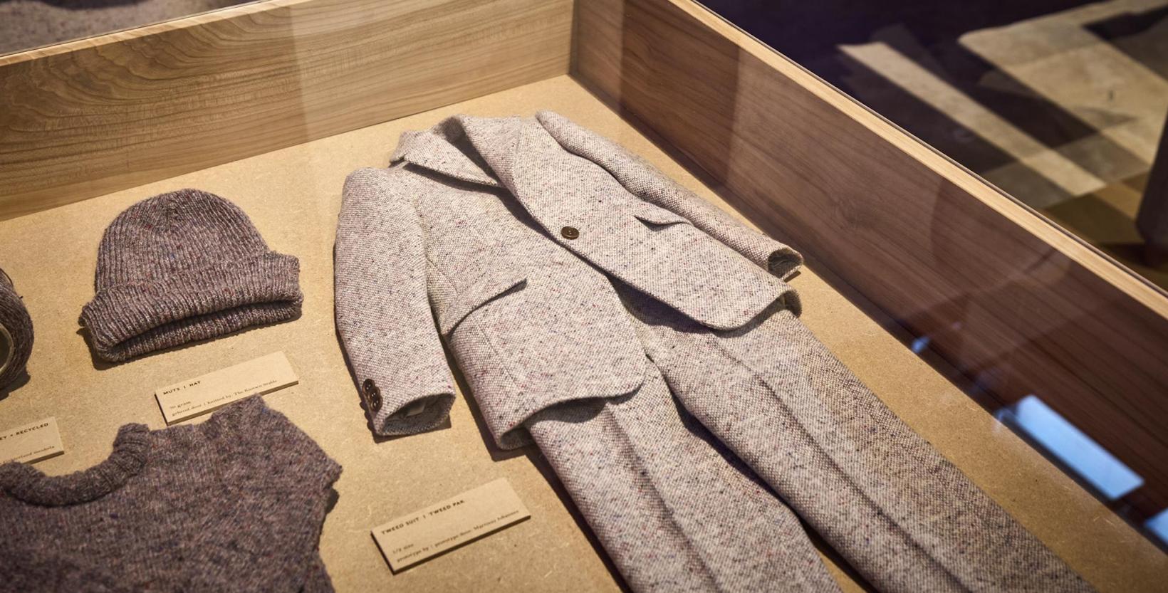 vitrine met daarin liggend een grijze wollen pak (colbertjas en broek), donker grijze wollen muts en truitje