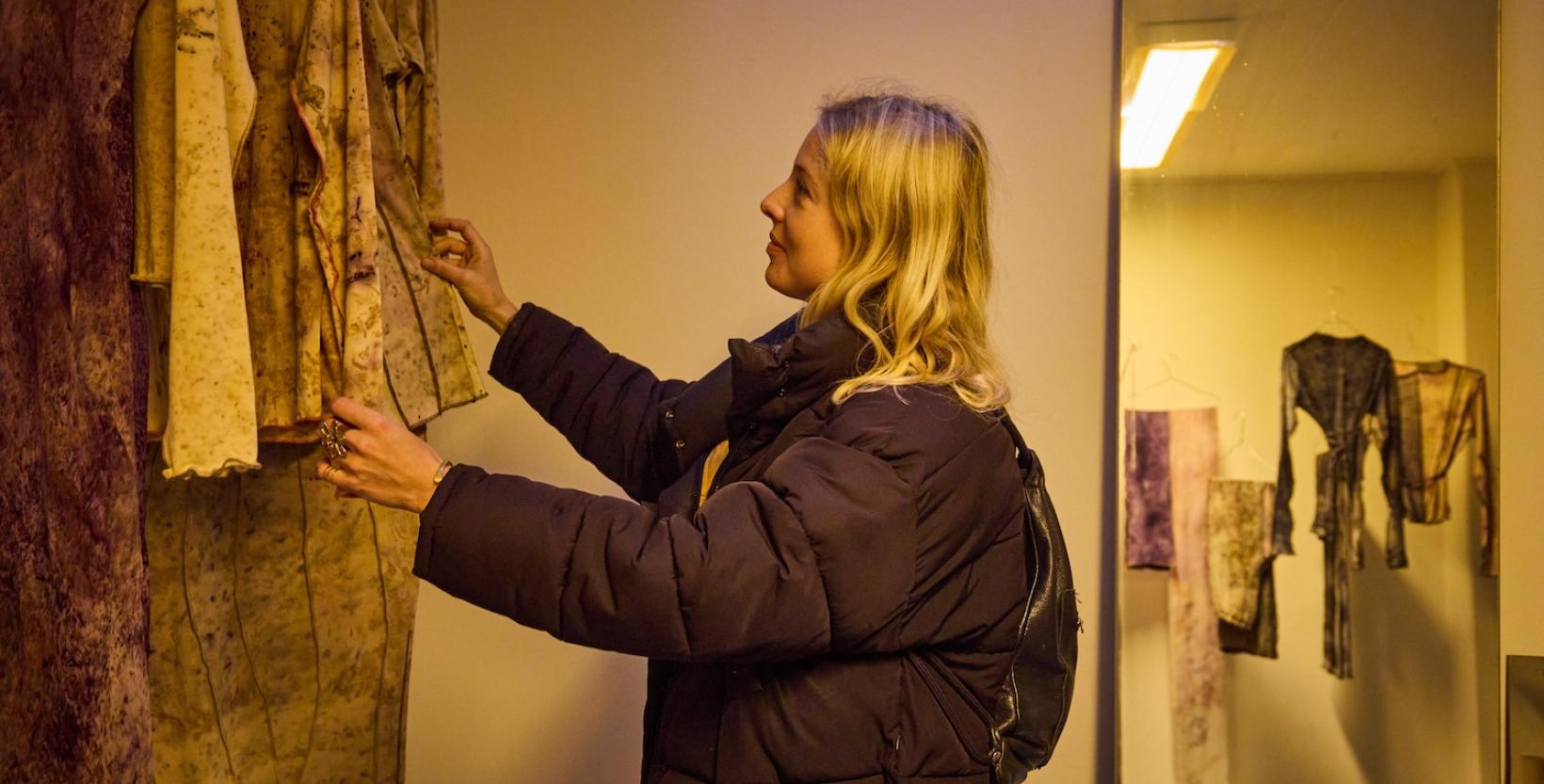 Bezoeker bekijkt kledingstukken van natuurlijk geverfde stoffen die als onderdeel van een tentoonstelling worden gepresenteerd.