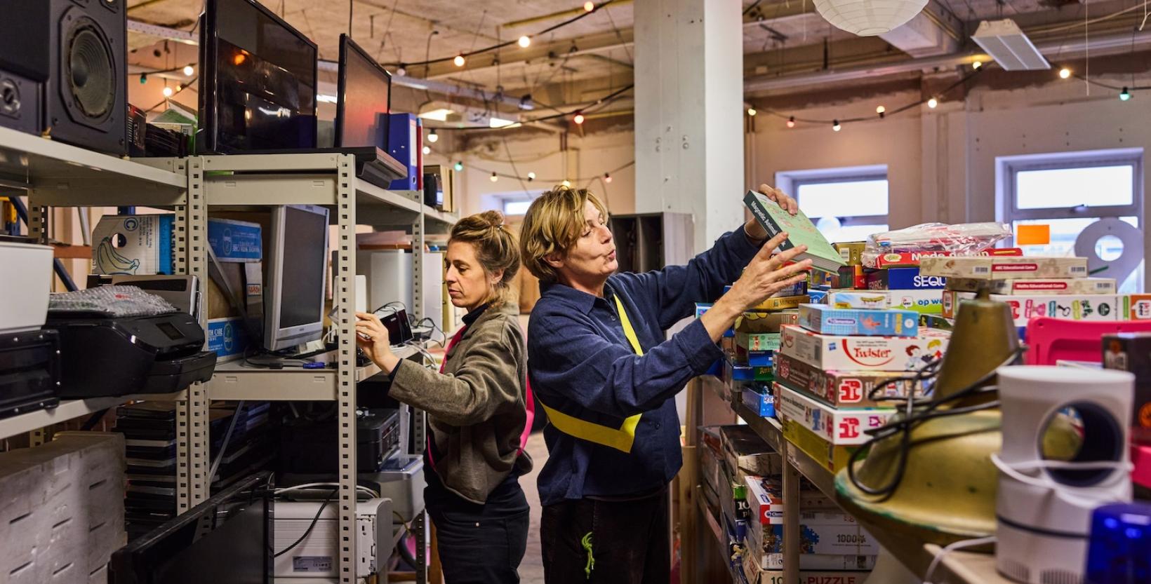 Vrijwilligers sorteren tweedehands spullen zoals elektronica en spellen in een weggeefwinkel.
