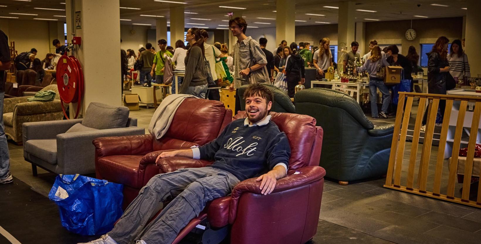 Studenten lopen rond tussen tweedehands meubels die zijn uitgestald in een grote hal.
