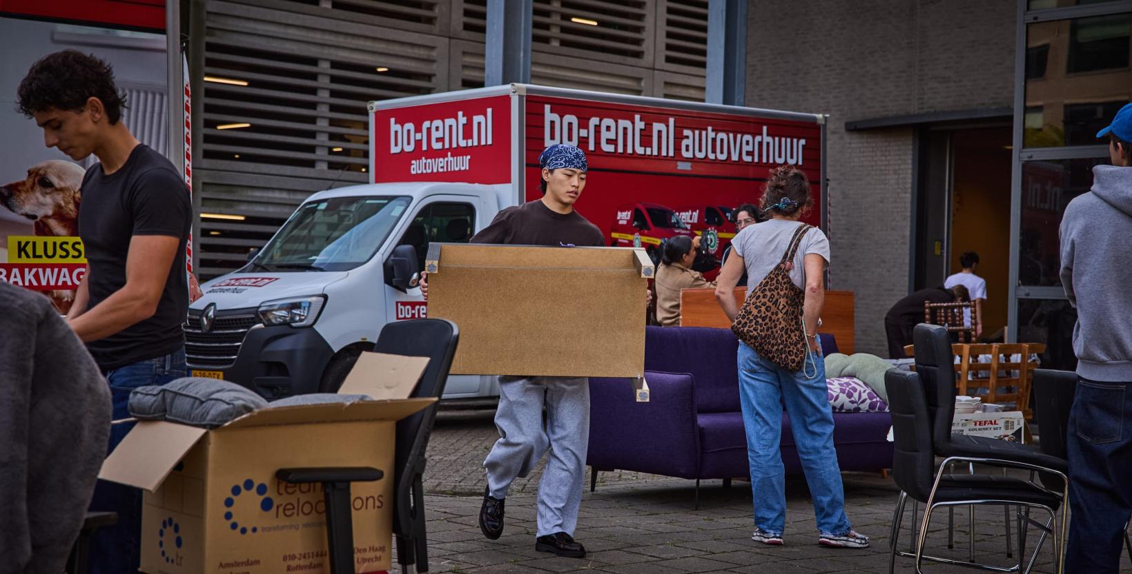 Studenten lopen rond tussen tweedehands meubels die zijn uitgestald in een grote hal.